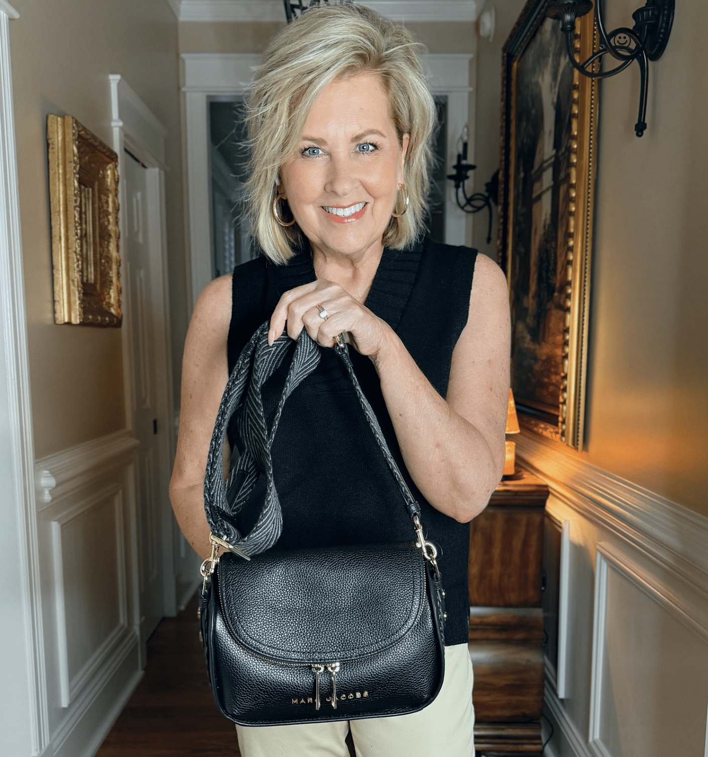 Woman wearing a long black sweater vest for summer and holding a black crossbody